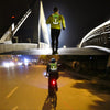 Person wearing a high-visibility safety vest on a bridge and a road at night.