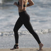 Person running on a beach wearing black leggings and a sports bra.