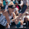 Woman playing paddle ball with a racket, wearing a visor and sports attire, in an outdoor setting.