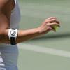 Person holding a tennis ball with a wristband featuring a logo on a blurred background